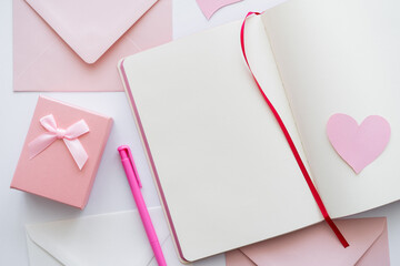 top view of notebook with paper heart near envelopes and gift box on white.