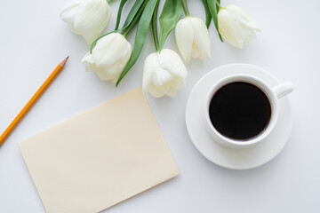 top view of envelope with pencil near cup with coffee and tulips on white.