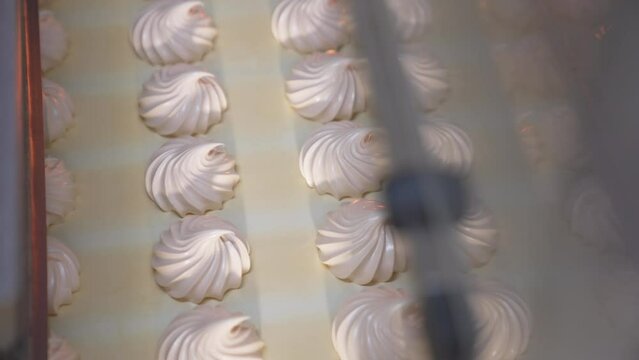 Delicious creamy marshmallow sweets moving slowly on the conveyor belt. Freshly-made vanilla desserts come out from machine. Close up. Top view.