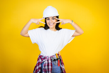 Young caucasian woman wearing hardhat and builder clothes over isolated yellow background Doing...