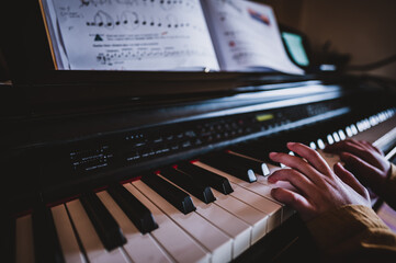 Young child practicing playing a piano with hands resting on keys