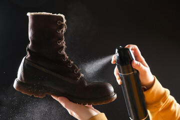 A woman applies the spray to brown nubuck women's winter boots. Water-repellent care for shoes,...