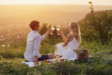 Summer picnic outdoors. Romantic happy couple is toasting glasses with wine and smiling. Romantic...