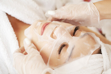 Fototapeta na wymiar Cosmetologist applying sheet mask on woman in spa salon