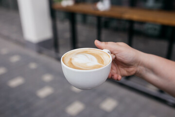 Woman holding latte art coffee on wooden table in coffee shop. Coffee in a mug.