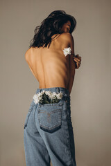 Woman from the back in jeans in a pocket with flowers, naked body, the concept of beauty, perfect...