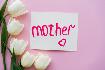 top view of white tulips near greeting card with mother lettering on pink.