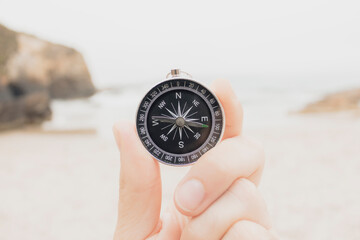 Closeup, hand holding an analog compass on the beach in front of the sea, concept travel, summer, selective focus.