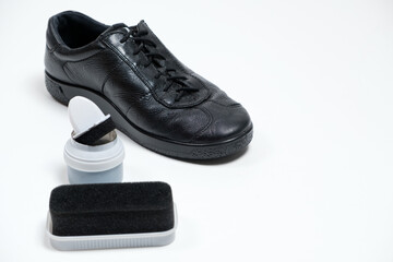 Shoe cream with sponge and black men's leather shoes on a white background. Shoe care, place for text.