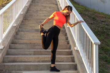 Young focused fitness girl in black yoga pants and orange short shirt work out and stretch her body...