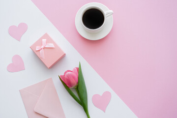 top view of envelope near cup with coffee, gift box and tulip on white and pink.