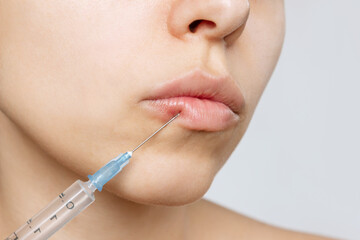 Cropped shot of young caucasian blonde woman's face with perfect lips with a syringe needle on lip....