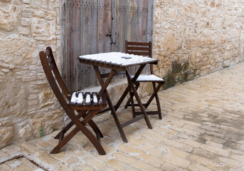 Fototapeta na wymiar Empty snow covered wooden chairs and coffee table on a stoned footpath.