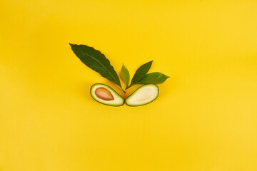 Fototapeta na wymiar Shot of a ripe avocado cut in half with leaves on a yellow background. Top view.