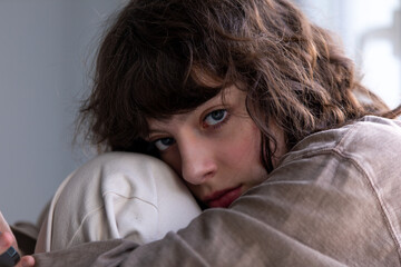 Portrait of a curly girl using a smartphone while sitting by the window.