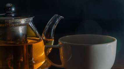 Picture of glass teapot with ceramic cup of green tea on dark background. Hot chinese green tea.