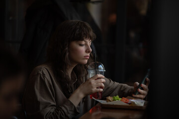 Young woman drinking lemonade and using smartphone in cafe.