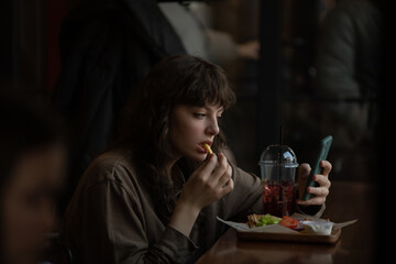 Young woman eating and using smartphone in cafe.