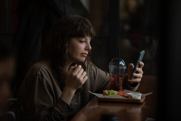 Young woman eating and using smartphone in cafe.