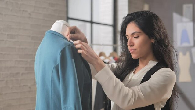 female latin tailor fashion designer working in studio draping dress on mannequin,hispanic woman dressmaker puts pin on blazer