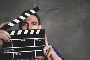 Man is holding clapperboard or clipboard in hands. Guy is directing and filming some cinema movie.