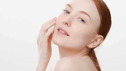 Close-up shot of young attractive slim ginger Caucasian woman touches her face and looks at camera on white background | Wrinkles prevention concept