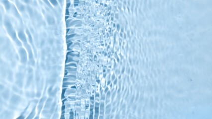 Single wave of water creates ripples and bubbles spontaneously on pale blue background | Beauty products background shot for advertising