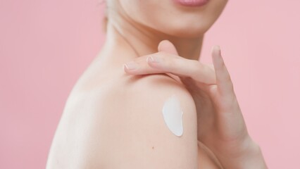 Obraz na płótnie Canvas Close up body part of beauty model applies moisturizing cream on her shoulder against pink background | Skin and body care commercial concept