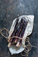 Fresh bunch of purple asparagus on packaging paper on a dark wooden background. Healthy food...