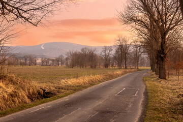 Fototapeta premium Sunset evening in the Pogórze Izerskie area in Poland in the early spring landscape with some trees and lonely road