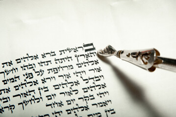 A silver yad points to the opening text of the Hebrew Bible, showing the first word of the first...