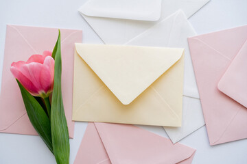 top view of pink tulip near pastel envelopes on white.