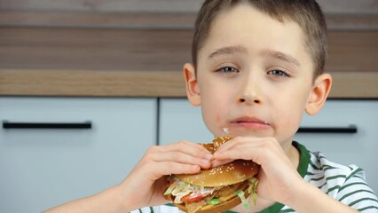 The child's face. A cute happy boy with an appetite bites a delicious burger. Fast food. The concept of food delivery. Food for lunch. A delicious burger