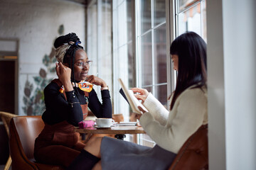Two multicultural female students sitting in cafeteria and study for exam.
