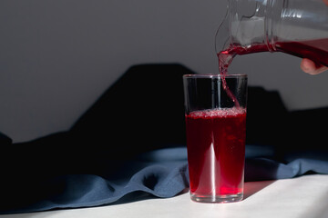 Pour red berry compote from a glass jug into a glass on a blue background