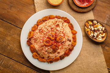 Masfouf from couscous with dried fruits in a plate on a wooden table next to saffron, and couscous groats in a bowl on a linen napkin.