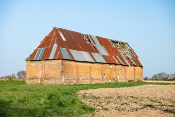 Batiment agricole ancien en brique rouge avec toiture en zinc dans une prairie