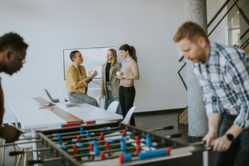Young casual multiethnic business people playing table football and relaxing at office