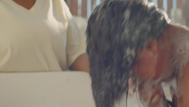Handheld camera shot of little African American boy diving into bathwater and then taking towel while bathing with mom at home