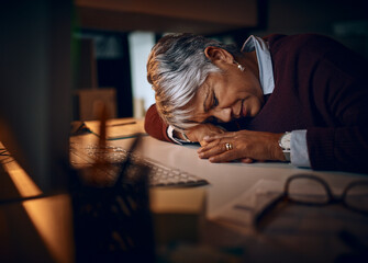Fototapeta na wymiar I just need a quick snooze.... Shot of a mature businesswoman sleeping at her desk while working late in an office.