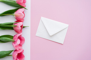 top view of envelope near blossoming tulips on white and pink.