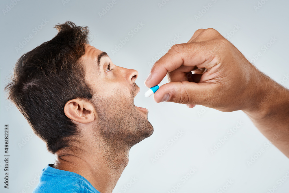 Poster open wide. studio shot of a carefree young man receiving a pill from an unrecognizable person while 