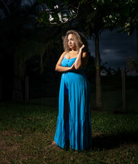 Brunette woman wearing a blue dress in a green area with trees in a heavy early evening. Wearing winter boots. Mention of female empowerment and attitude.