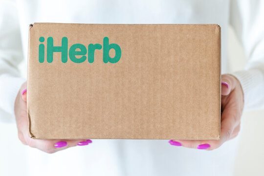 iHerb cardboard box in woman hands. Delivery of goods in a cardboard box