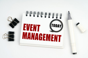 On a white surface lies a marker, clips and a notebook with the inscriptions Today and EVENT MANAGEMENT