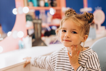 Portrait of a little beautiful girl with a stylish hairstyle in a beauty salon, expressing...