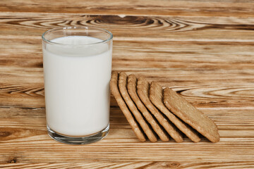 Glass of fresh milk and sweet cookies on wooden table.