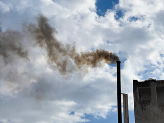 Fototapeta na wymiar Smoke from a pipe on a background of a blue cloudy sky
