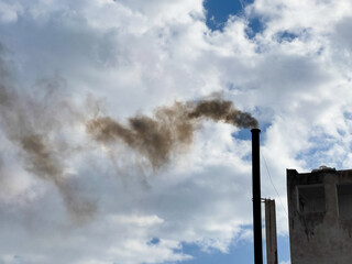 Fototapeta na wymiar Smoke from a pipe on a background of a blue cloudy sky