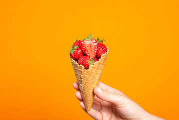 Hand holding waffle cup with ripe fresh strawberries on orange background